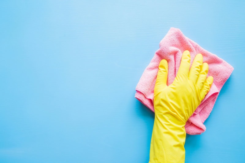 Does An AC Kill Mold? Hand in a yellow rubber glove wiping a blue wall or table with a pink cloth