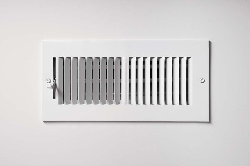 A heating/cooling vent register on the wall of a home, with open/close lever.