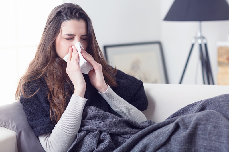 Blog Title: What Does Indoor Air Quality Have to Do With Allergies? Photo: Woman sneezing into a tissue