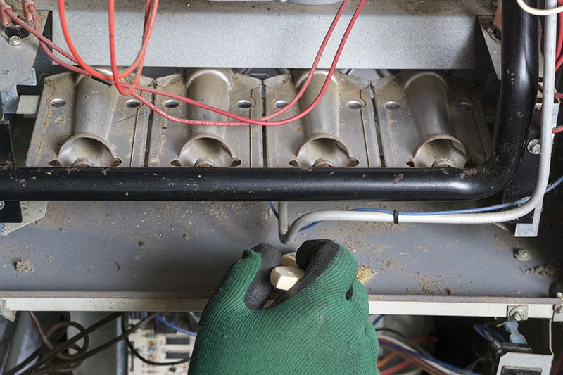 Image of someone checking a furnace with green gloves. 5 reasons to schedule a fall furnace clean and check.